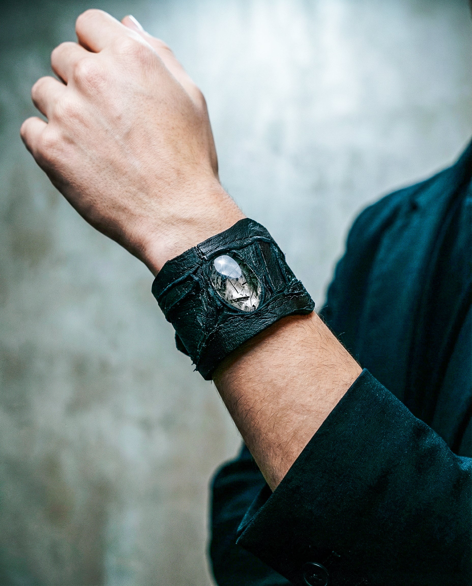 Person wearing a dark leather wristband with a stone on a blurred background